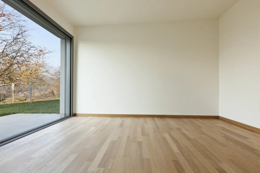 Lege ruimte met houten vloer en een brede raampartij naar de tuin